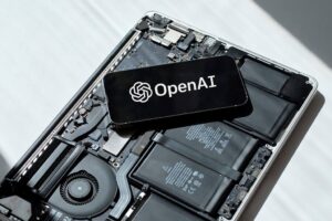 A phone with the OpenAI logo on it, sitting on the internals of an opened-up laptop without the casing