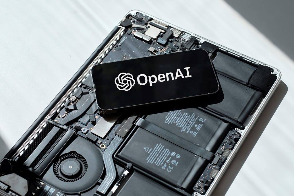 A phone with the OpenAI logo on it, sitting on the internals of an opened-up laptop without the casing