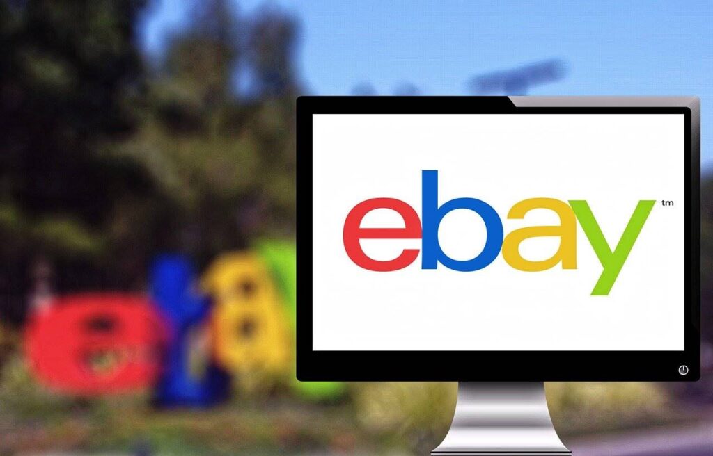 A computer screen with the eBay logo on it, with an eBay logo sign in the blurred background