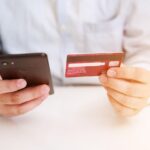 A person holding their phone in one hand, with a credit or debit card in the other