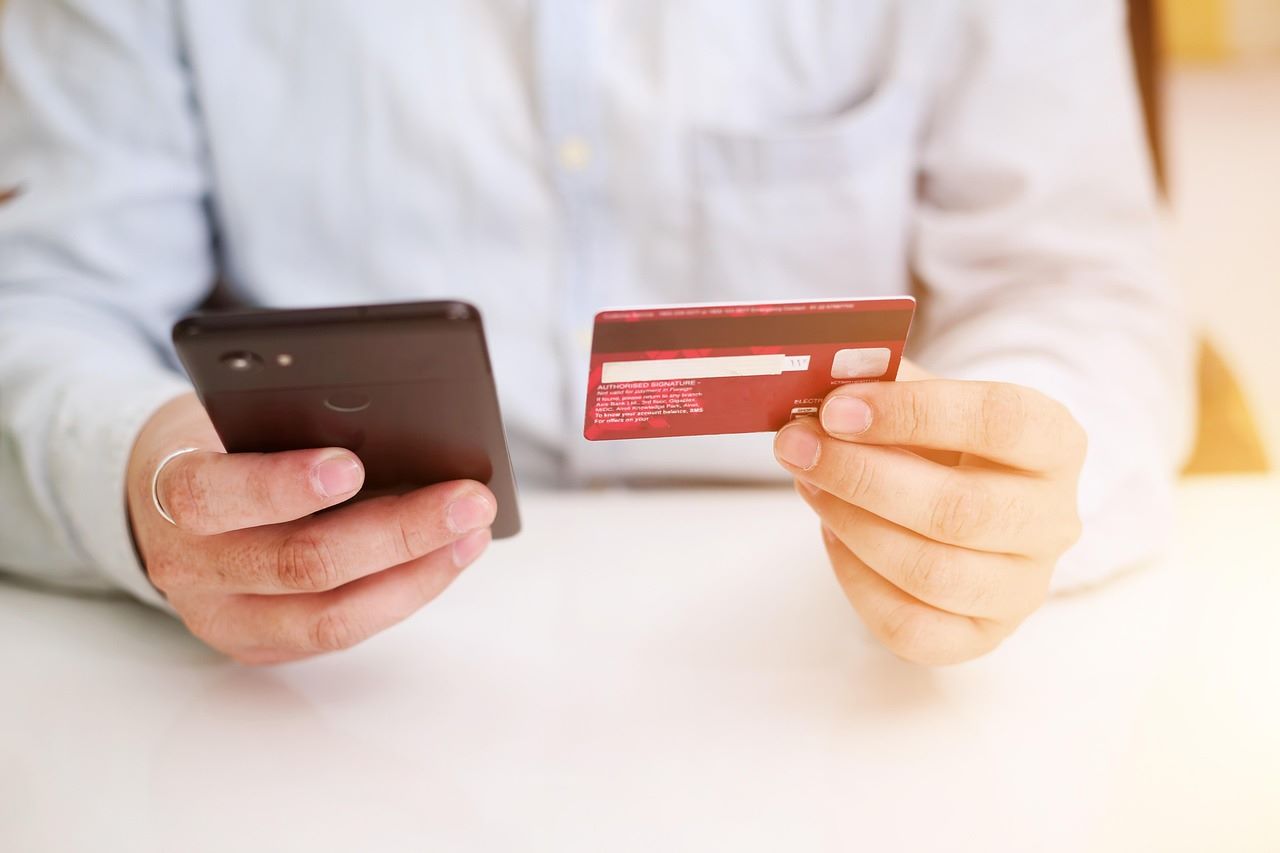 A person holding their phone in one hand, with a credit or debit card in the other