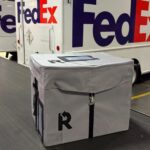 An image of a reusable shipping box next to some FedEx vehicles