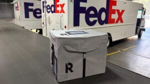 An image of a reusable shipping box next to some FedEx vehicles