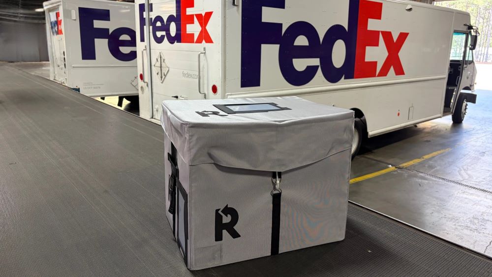 An image of a reusable shipping box next to some FedEx vehicles