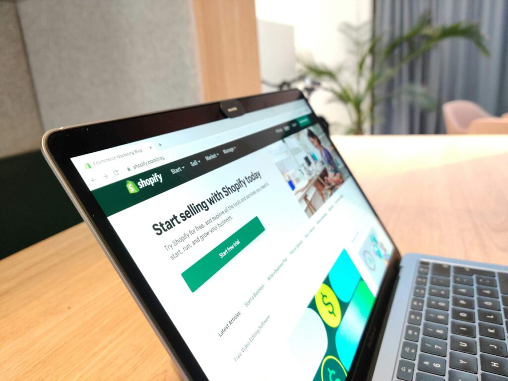 Shopify ecommerce platform visible in the MacBook Air on the wooden table.