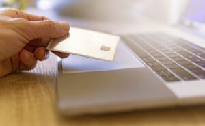 A person holding a debit or credit card while sitting at their laptop
