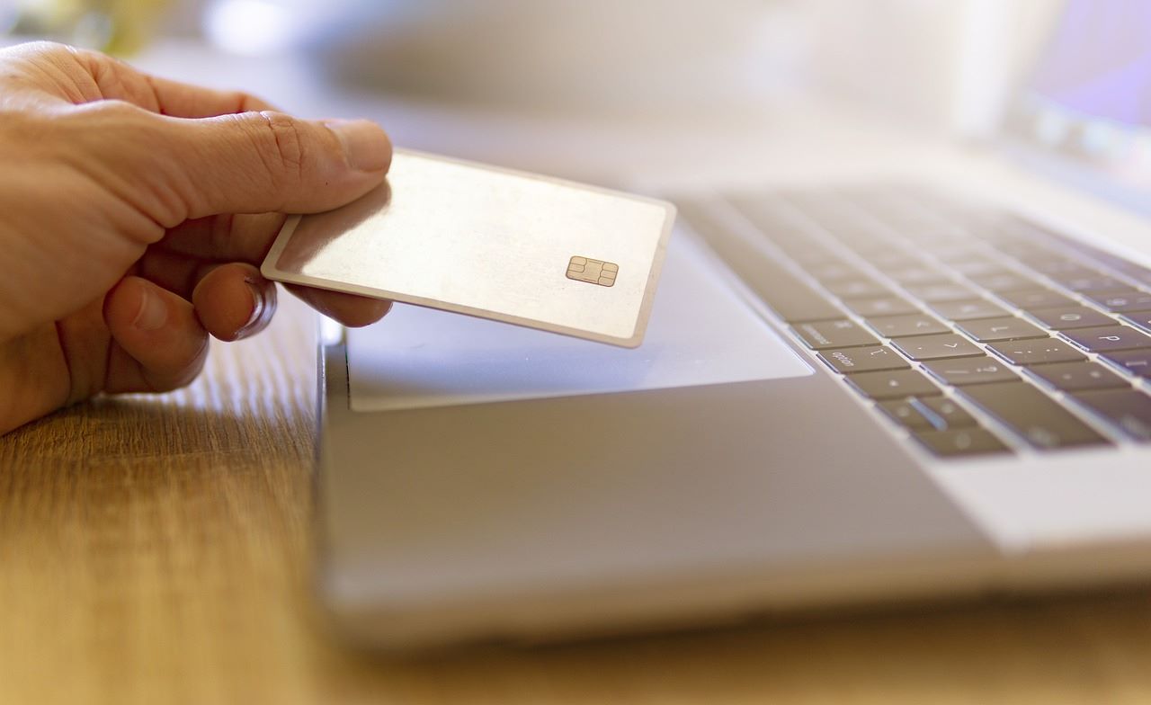 A person holding a debit or credit card while sitting at their laptop
