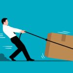 A person struggling to drag a large cardboard box with a rope tied around it