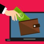 A hand putting money into a digital wallet on a laptop computer screen.