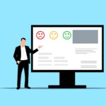 An image of a man standing next to a computer screen and gesturing towards it, with the screen having a sad, neutral, and happy face on it.