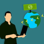 A person standing holding a laptop, next to the earth, which has a dollar bill above it and some arrows circling the planet.