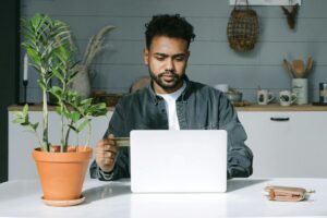 A man staring at his computer, typing, and also holding a credit or debit card in his hand