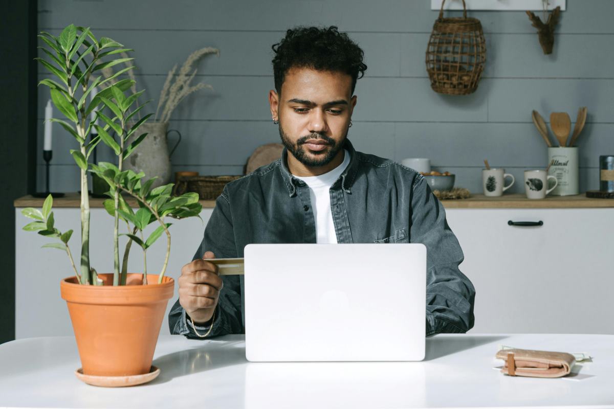 A man staring at his computer, typing, and also holding a credit or debit card in his hand