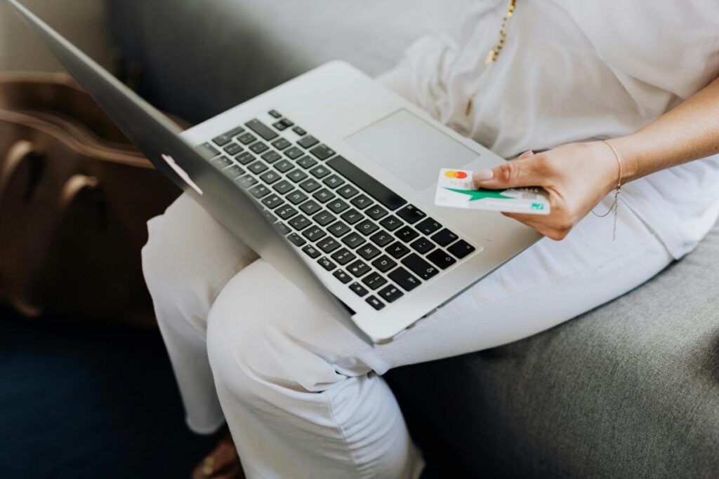 A person sitting on a couch with a laptop on their lap and a credit or debit card in their hand