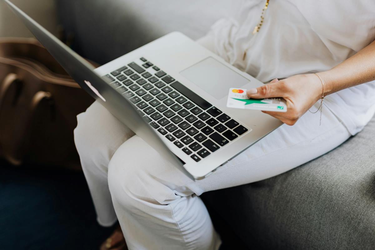 A person sitting on a couch with a laptop on their lap and a credit or debit card in their hand