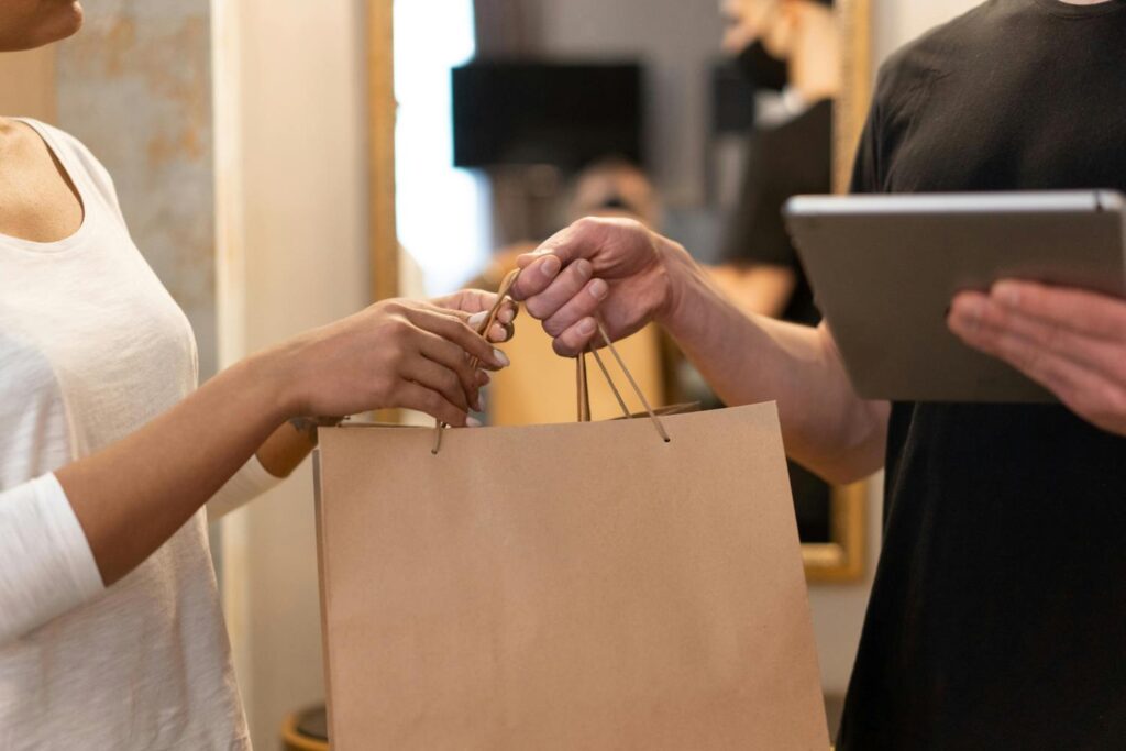 A person holding a tablet giving a paper bag to another person