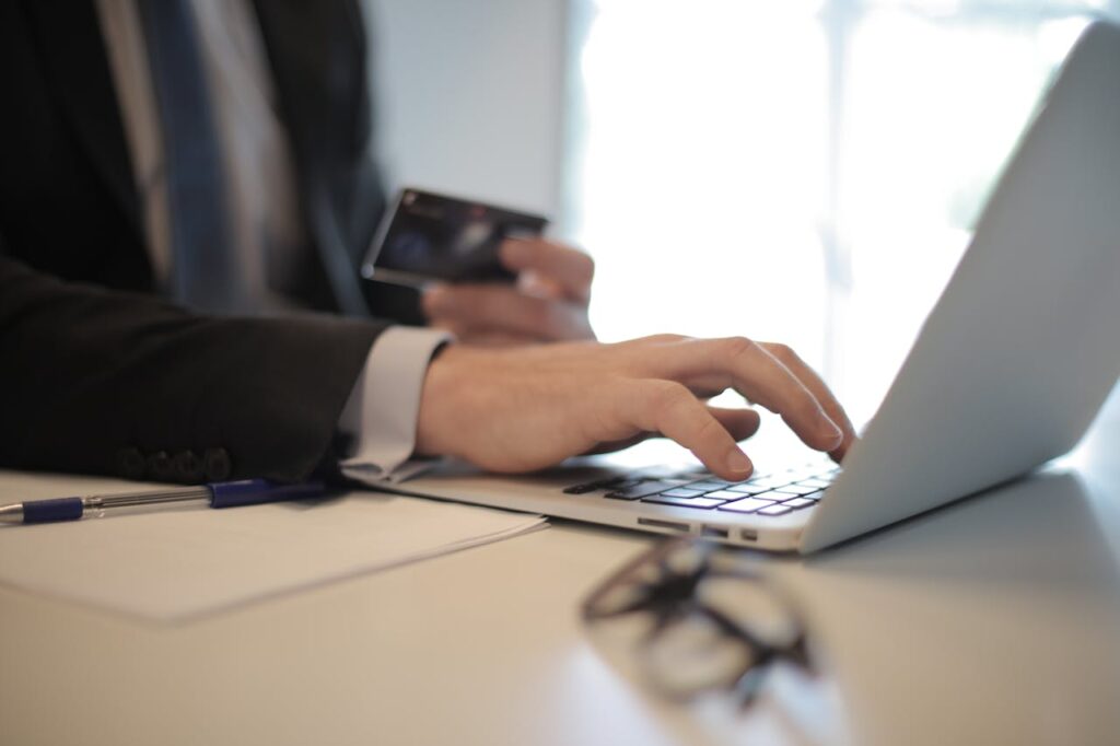 Person typing on a computer with a credit card in their other hand.