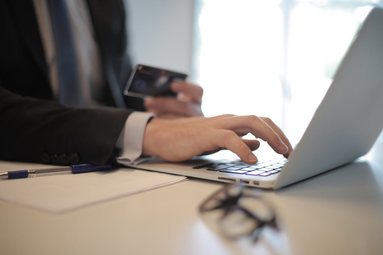Person typing on a computer with a credit card in their other hand.