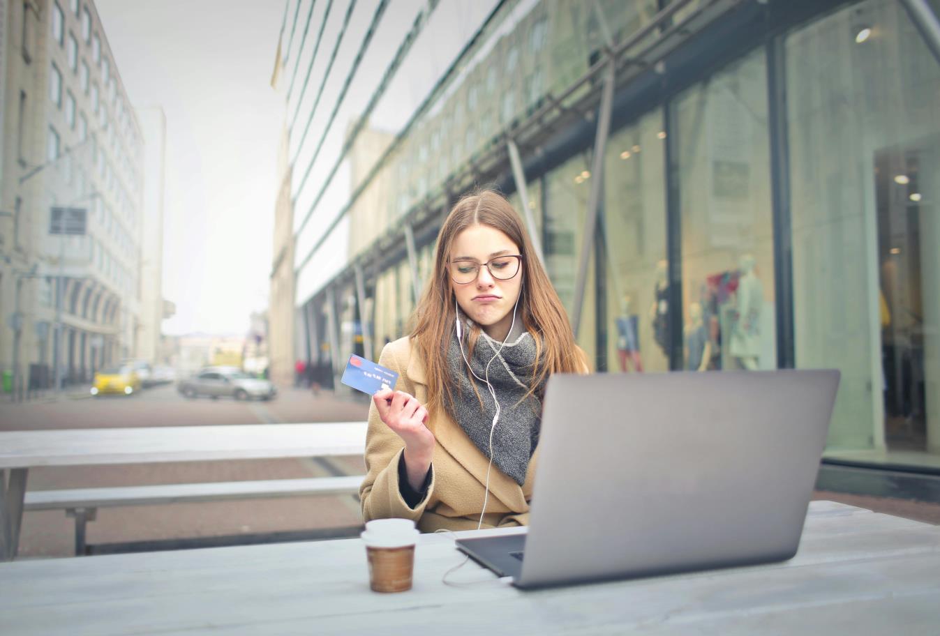 Woman in a coat sitting at a table with a laptop and holding a card