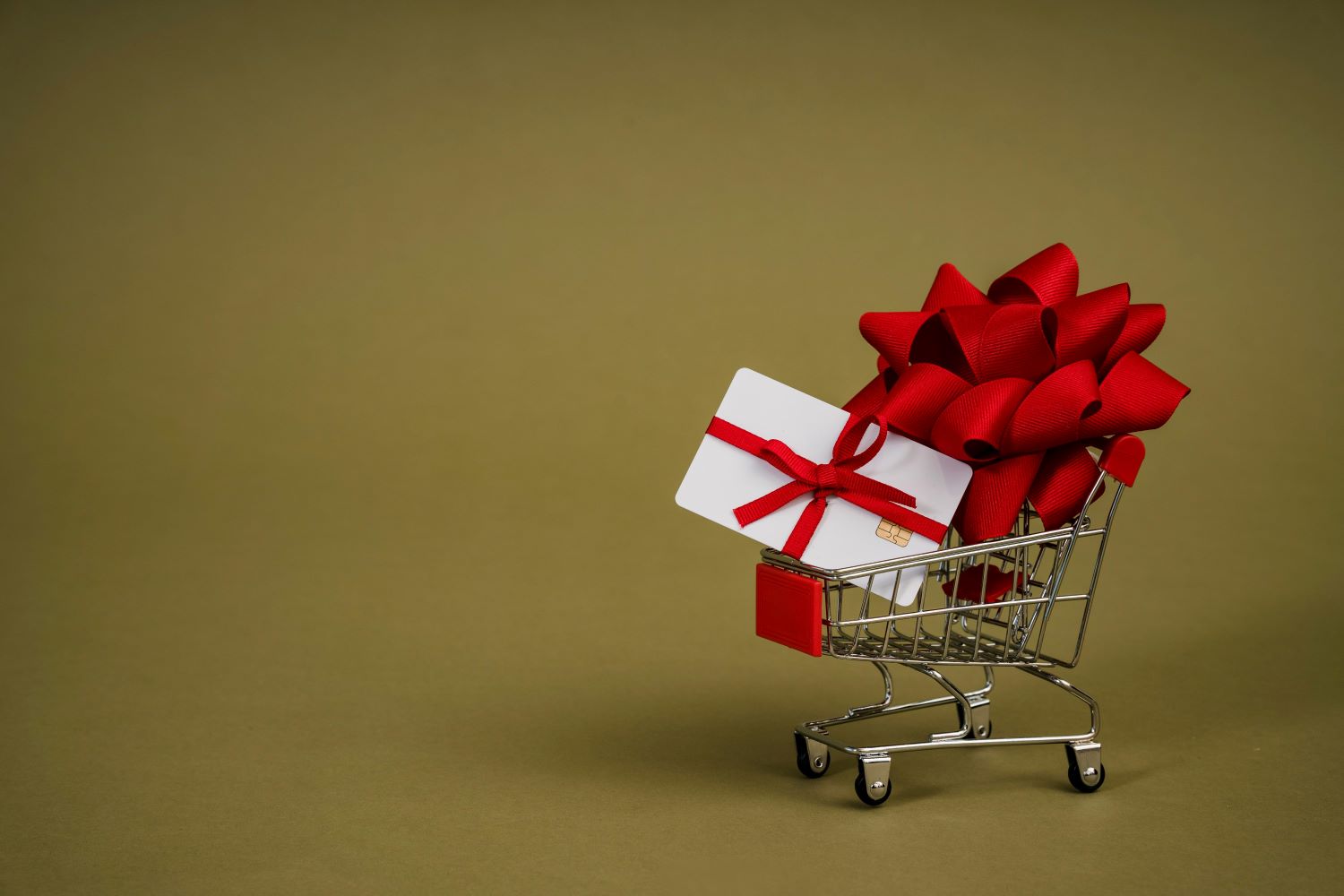 A shopping cart with a credit card wrapped in ribbon and a bow.