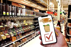 An image of a phone in a grocery store, with the phone screen showing a delivery vehicle, a bag of groceries, and a checkmark on it.