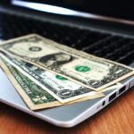 A few dollar bills on top of an open laptop