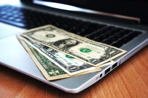 A few dollar bills on top of an open laptop